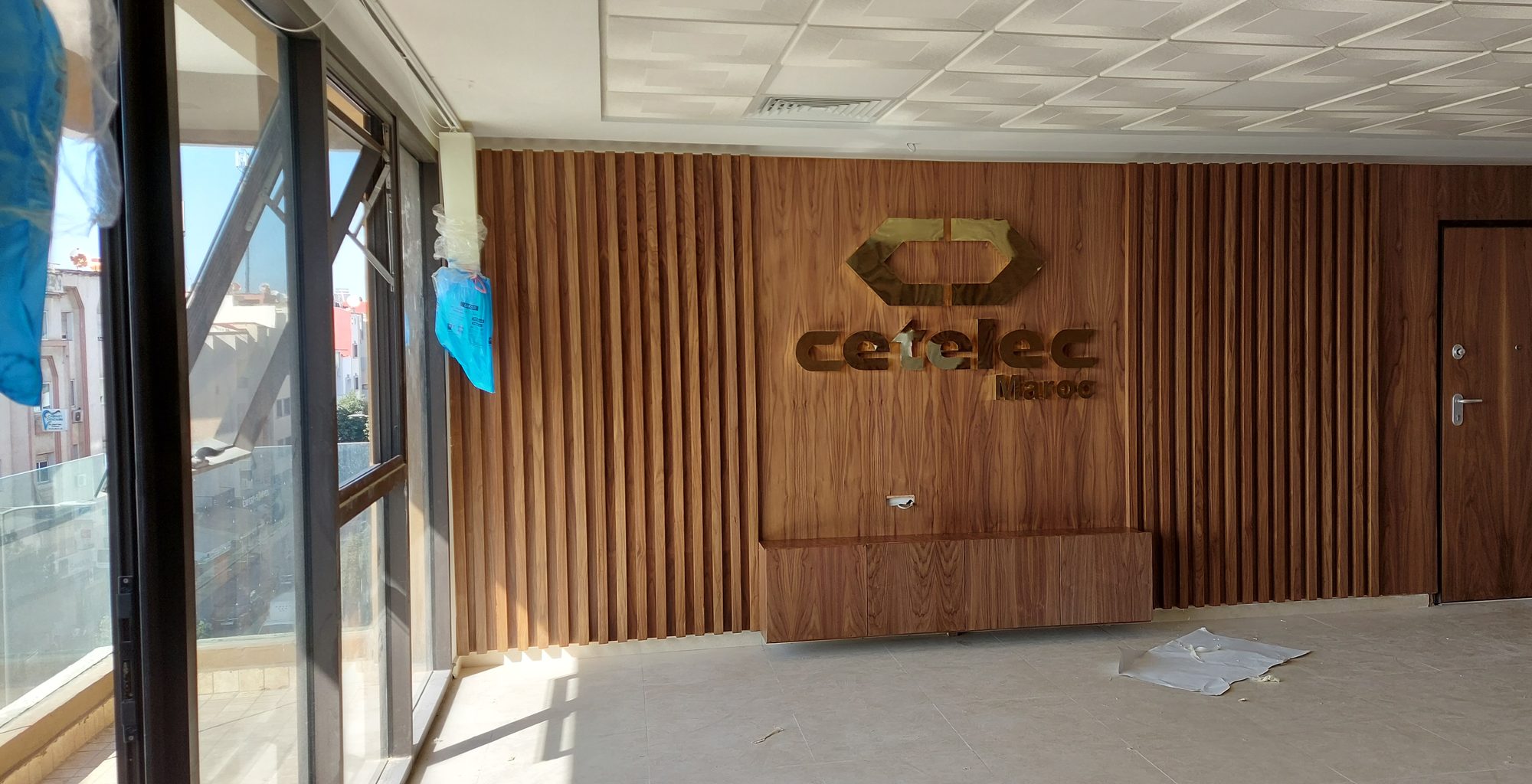 Cetelec Maroc main room with slatted wood feature wall, gold-finish logo and wall-hung cabinet
