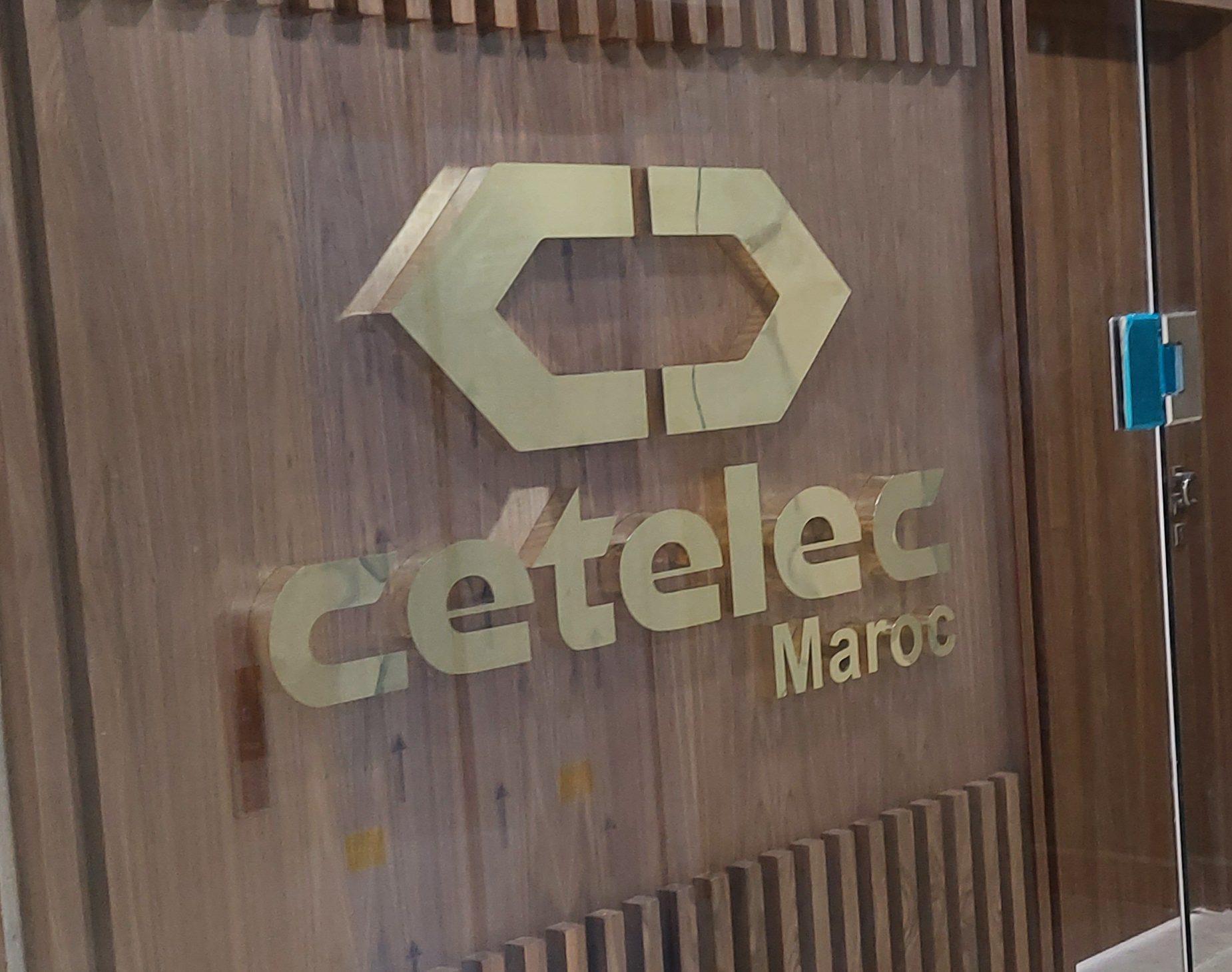 接待区木饰面墙上的金色 Cetelec Maroc 立体字