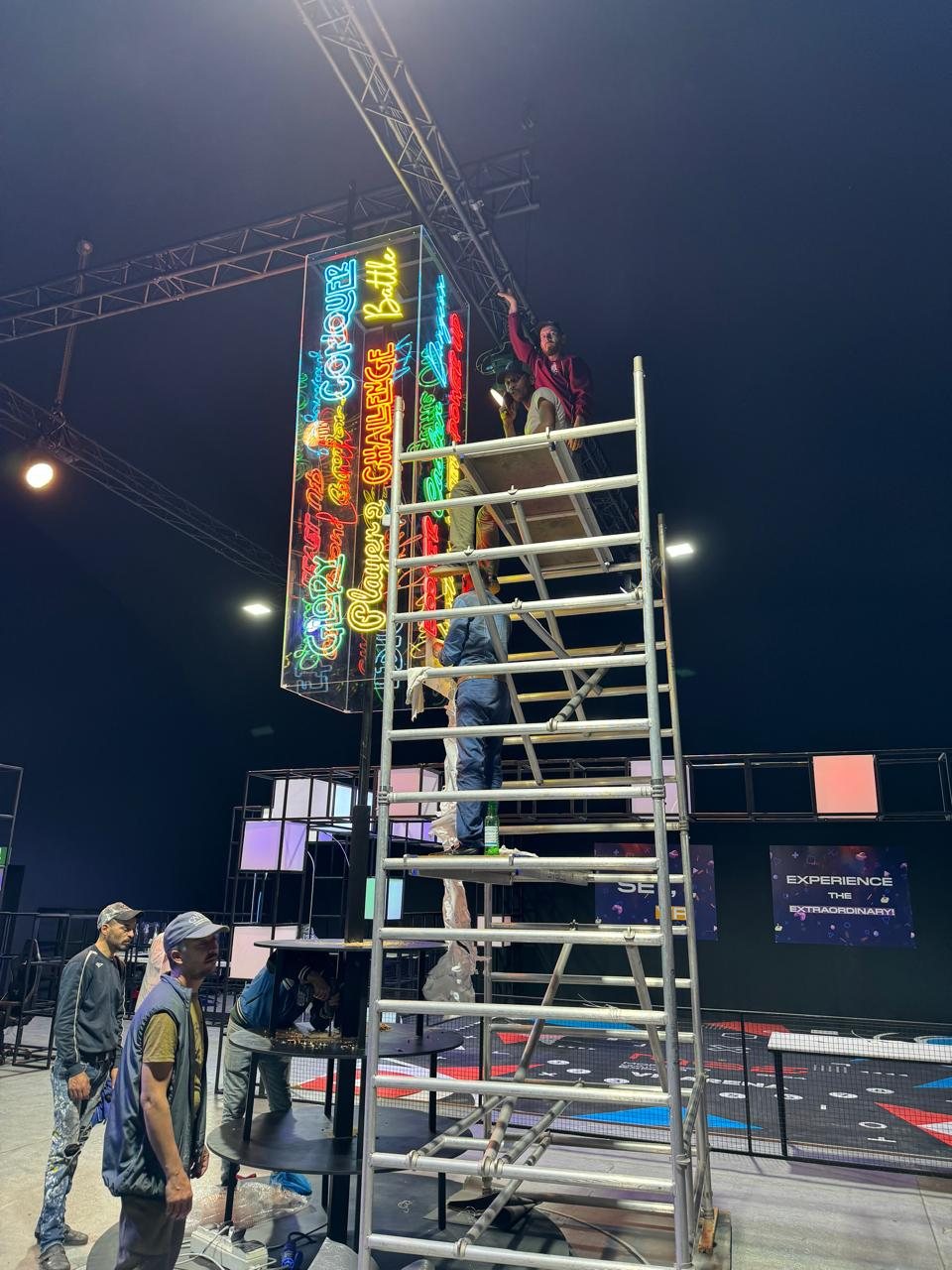 Neon tower of handwritten gaming words being finished on scaffolding