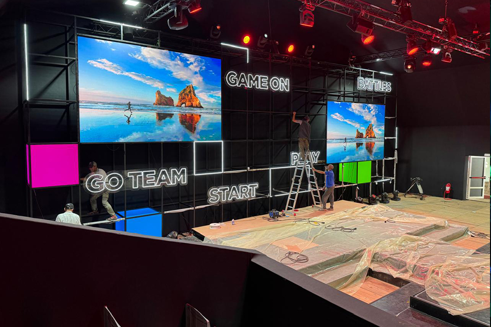 The full stage grid during installation, with LED screens, neon words and light boxes being fitted