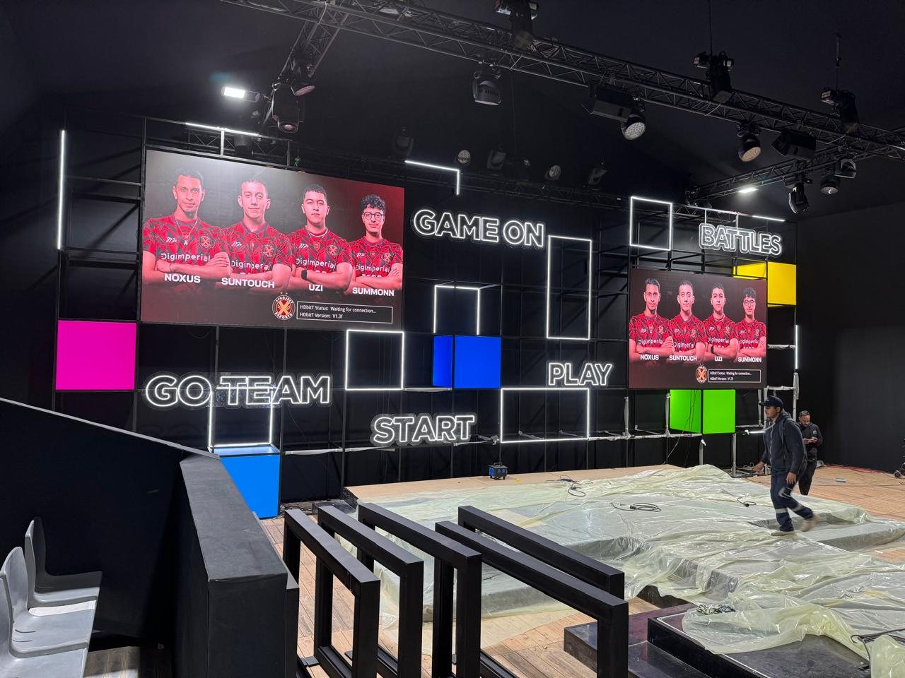 Main tournament stage with LED screens showing the team line-up, neon words and coloured light boxes on a black grid