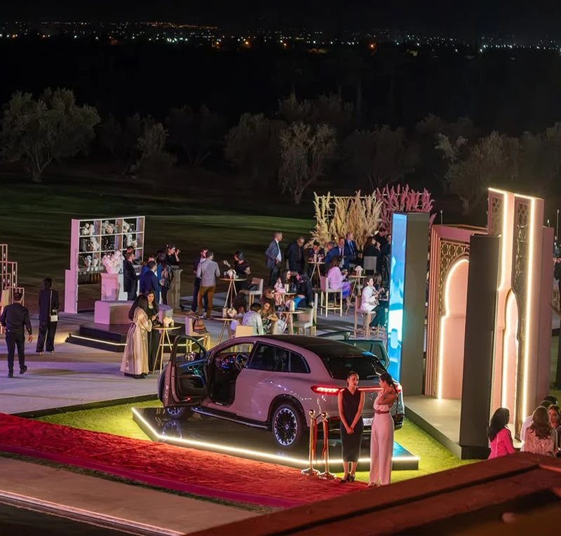 Evening view of the Mercedes-Benz EQS SUV showcase with illuminated platform, arches and guests