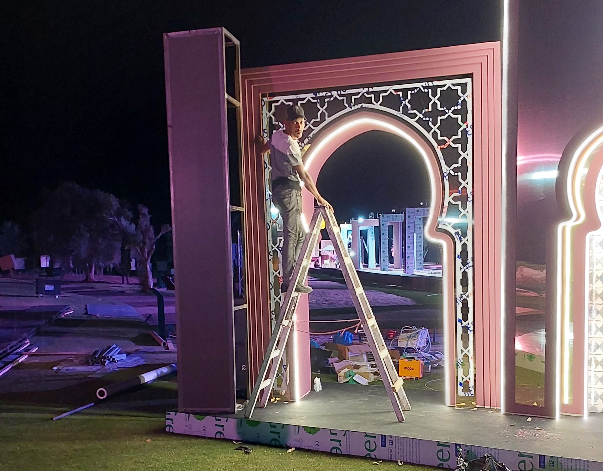 An installer finishing the lit arch at night before the opening