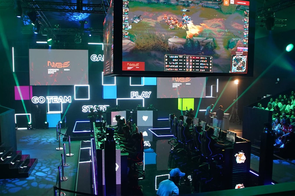 Esports tournament arena at Morocco Gaming Expo 2024 with neon-outlined stage, players and suspended screens